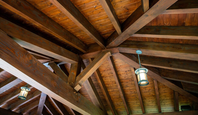Wooden ceiling with exposed beams and two hanging lantern-style lights. The wood planks have a rich brown finish, showcasing the structure and craftsmanship of the roof.