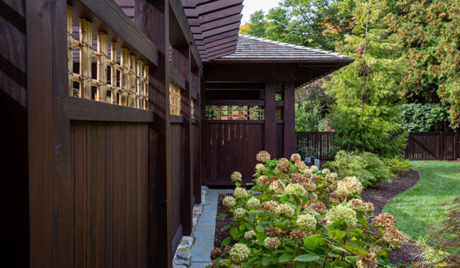 A wooden pergola with lattice panels stands beside a garden bed filled with blooming hydrangeas, surrounded by lush greenery and a well-maintained lawn.