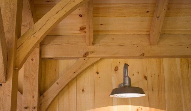A metal pendant light hangs from a wooden ceiling with exposed beams and natural wood paneling, creating a warm and rustic atmosphere.