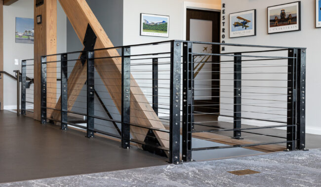 A modern staircase with black metal railings and wood beams is pictured indoors, with aviation-themed photos on the walls and a sign indicating the restroom in the background.