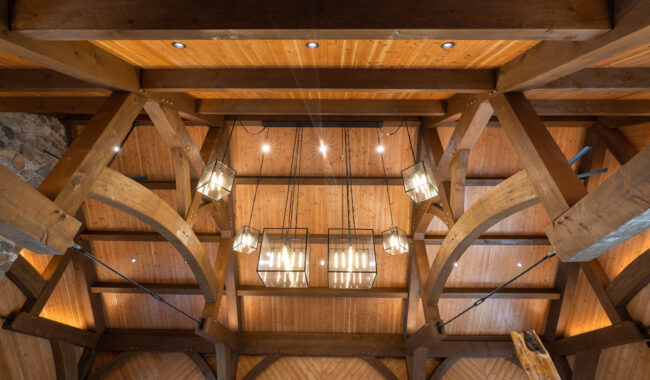 Ceiling view of a rustic wooden room with exposed beams, arched supports, and multiple modern pendant light fixtures hanging down, creating a warm and inviting atmosphere.