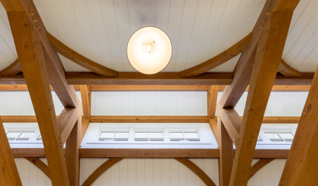 Wooden ceiling beams with a white panel ceiling, a round ceiling light in the center, and a horizontal row of small windows beneath the beams allow natural light into the space.