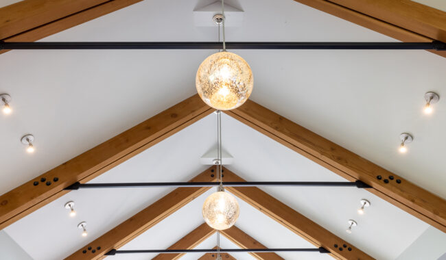 Ceiling with exposed wooden beams, black metal rods, and multiple round pendant lights hanging in a row, along with recessed ceiling spotlights on both sides.