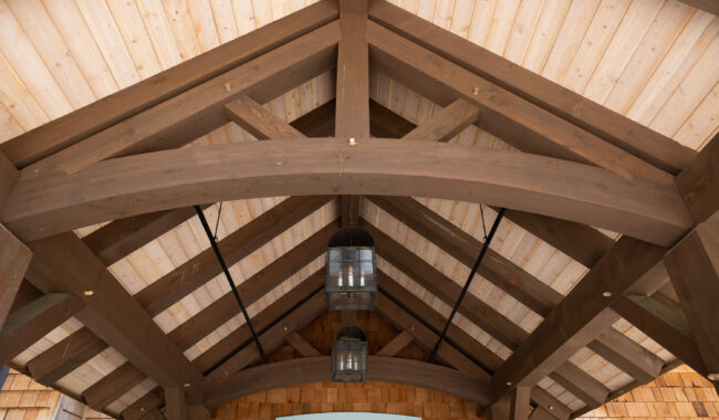 Wooden ceiling with exposed beams and two hanging lanterns. Below, a sign reads Jane Clifton Ashford Center. The structure features light wood planks and brown beams in a peaked roof design.