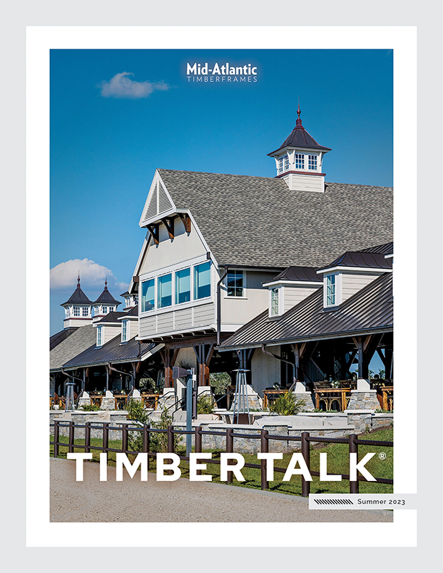 A large timber-frame building with a steep roof, cupolas, and outdoor seating, under a blue sky. The text reads “Mid-Atlantic Timberframes,” “TIMBER TALK,” and “Summer 2023.”.