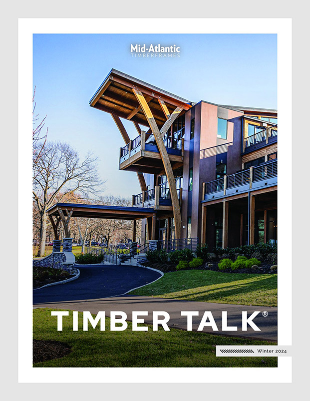 Modern timber-framed building surrounded by grass and leafless trees, featured on the cover of Timber Talk magazine, Winter 2024 edition, by Mid-Atlantic Timberframes.