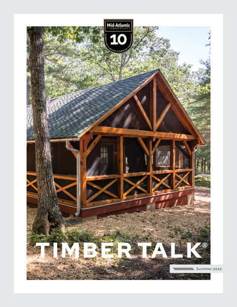 A wooden cabin with a screened porch stands among trees, featured on the cover of Timber Talk magazine, Summer 2022 edition, with a Mid-Atlantic 10 badge at the top.