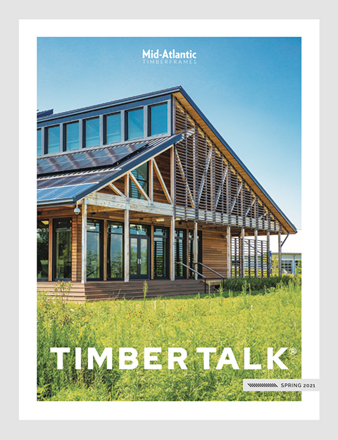 A modern timber-frame building with large windows and a slanted roof, set amid green grass, is featured on the cover of Timber Talk magazine, Spring 2021 edition by Mid-Atlantic Timber Frames.