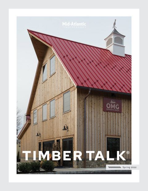 A rustic wooden barn with a bright red metal roof and a small cupola, featured on the cover of Timber Talk Spring 2022 issue, with the sign OMG and Mid-Atlantic text above the roof.